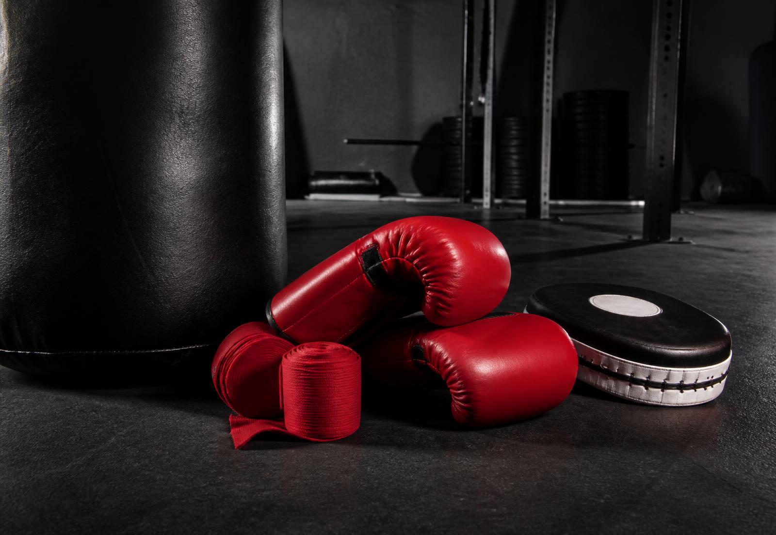 Luvas de boxe, bandagens e manoplas ao lado de um saco de pancadas
